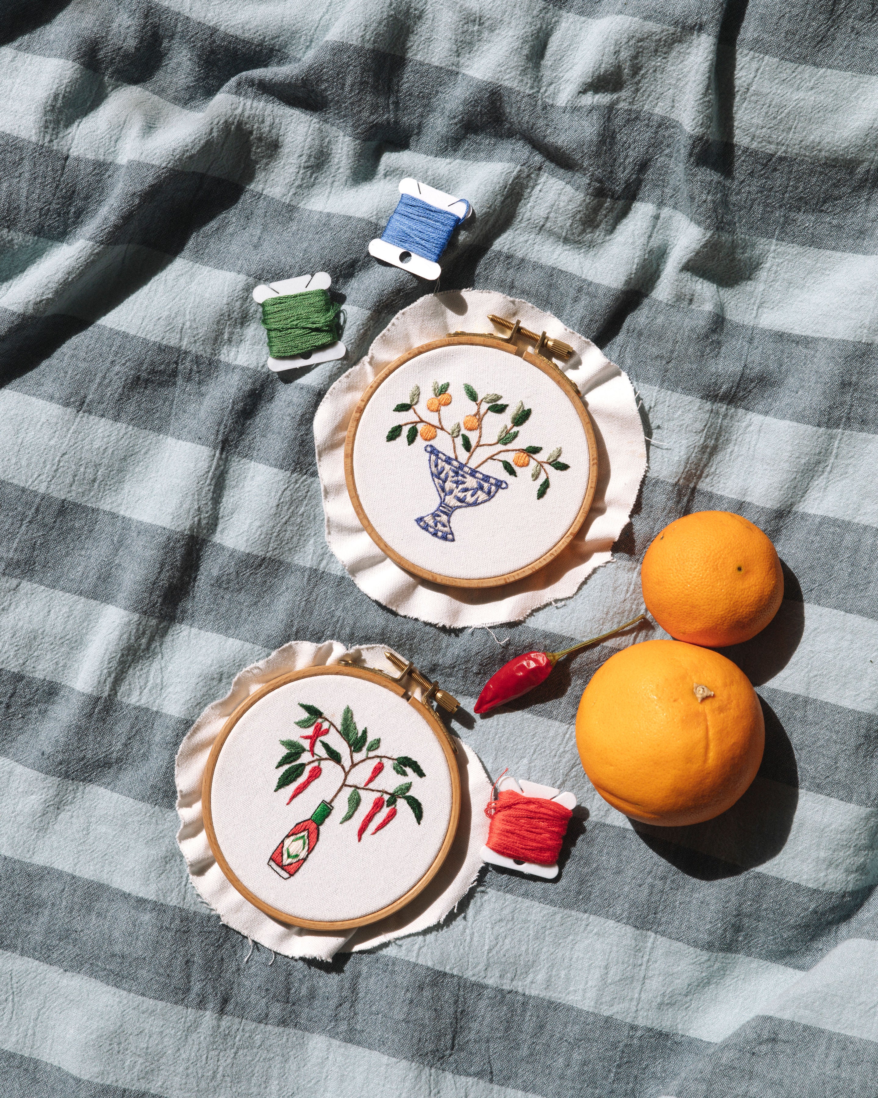 Mini Italian Vase embroidery hoop art with floral design on checkered fabric, displayed with oranges and colorful thread spools