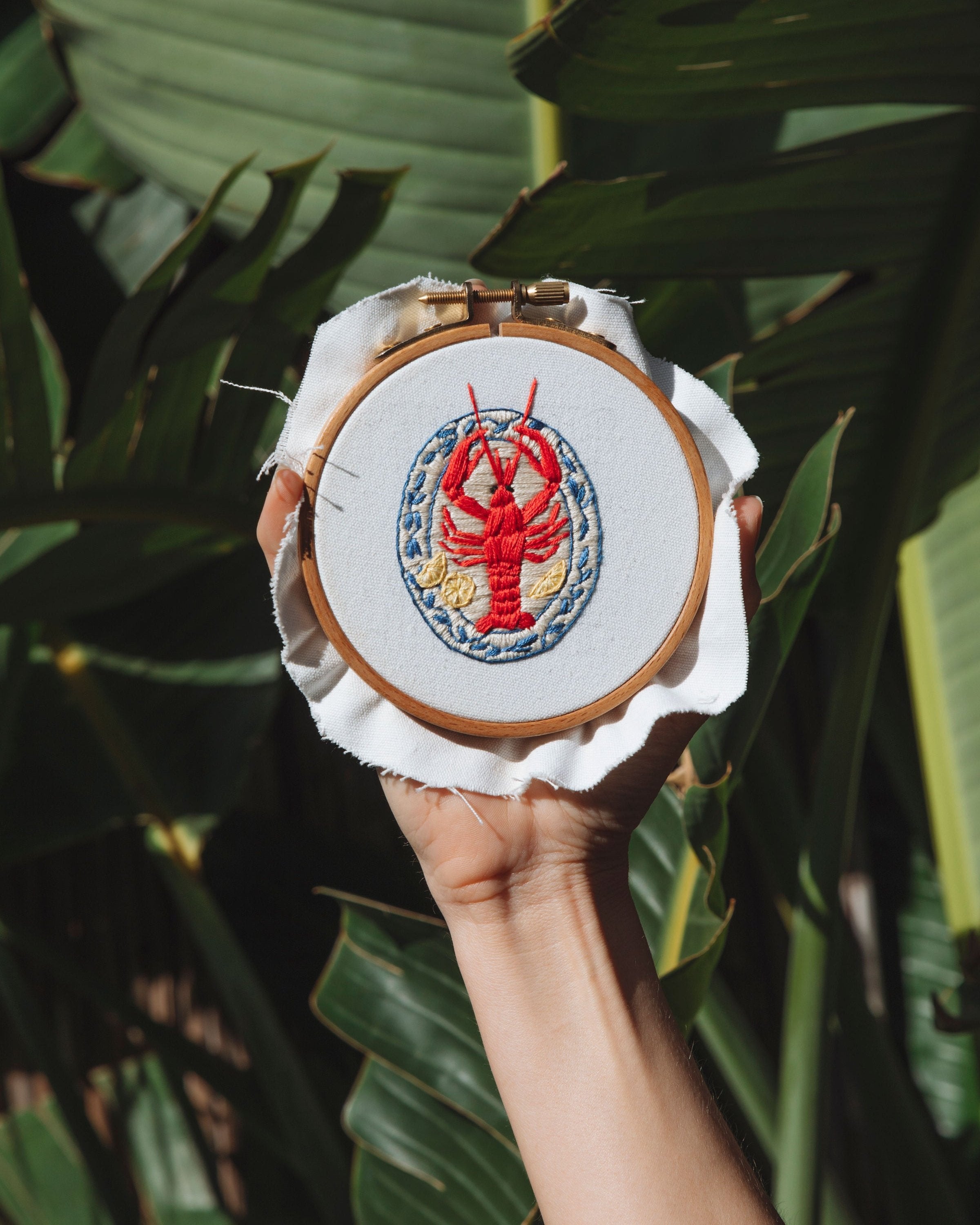 Mini Italian Collection embroidery hoop featuring red lobster design on white fabric against tropical leaves background