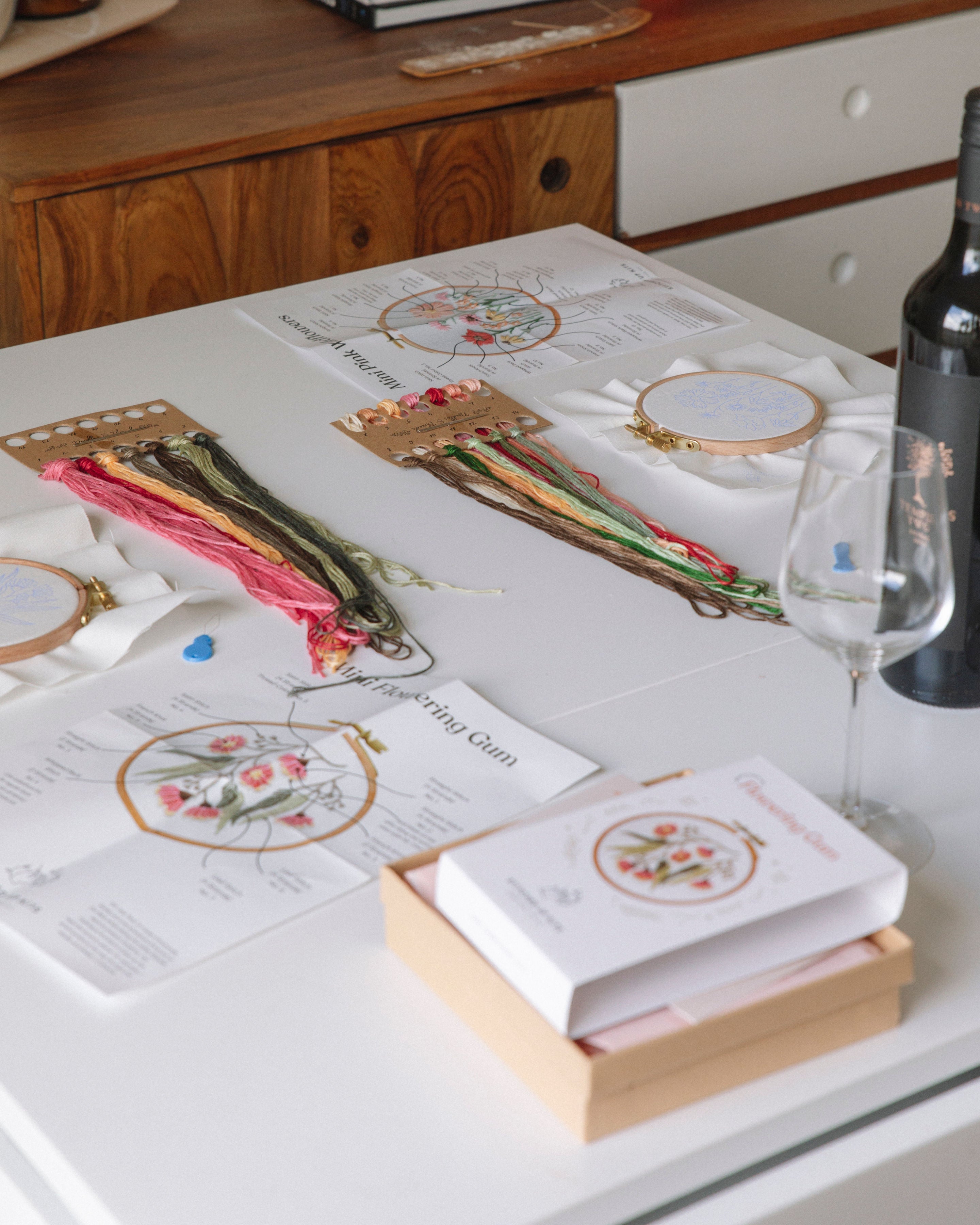 Mini Italian Vase surrounded by embroidery supplies, thread skeins, and craft materials on white table with wooden backdrop