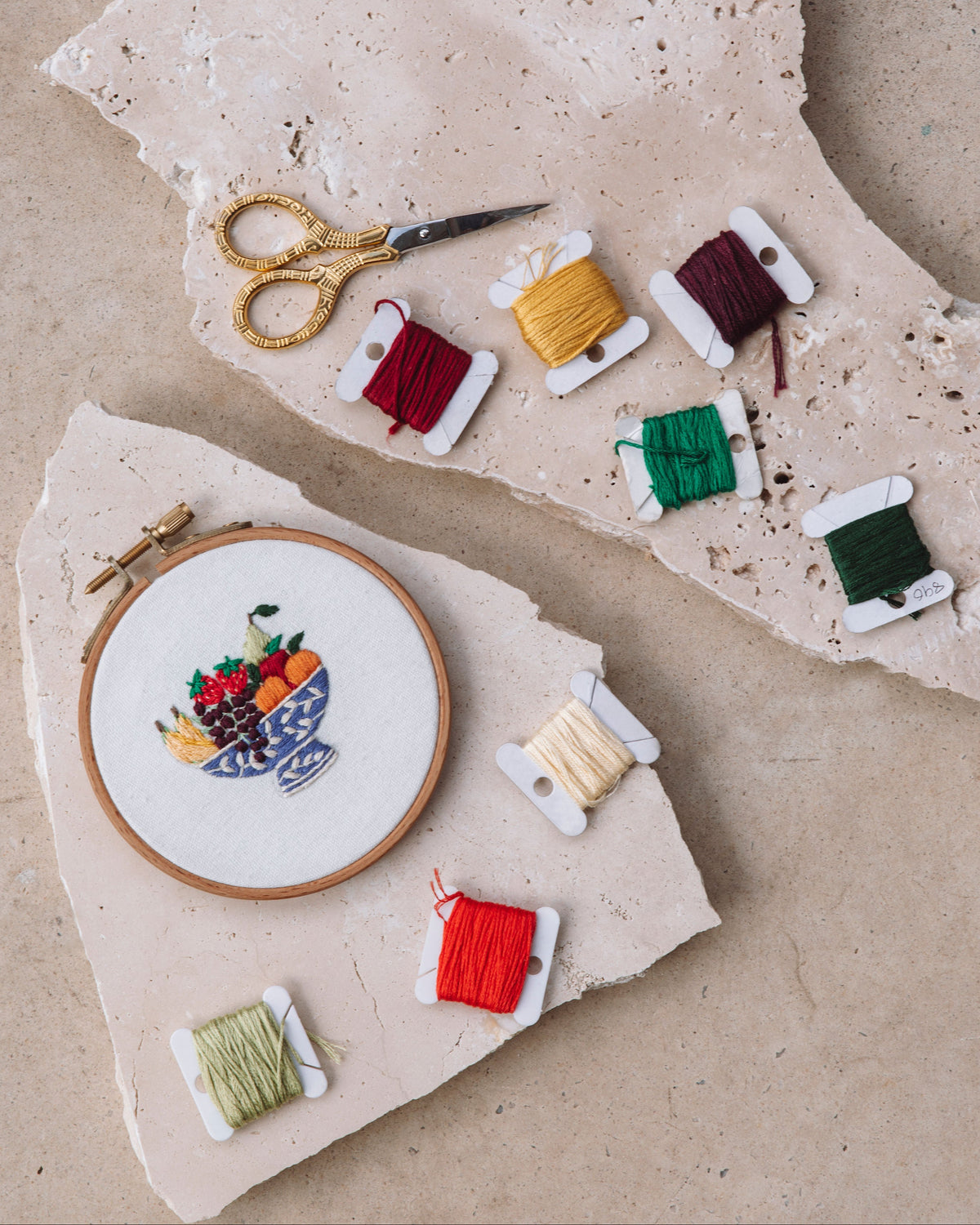 Girls Stitch Night Bundle showing embroidered fruit bowl in wooden hoop with colorful threads and vintage scissors on stone slabs
