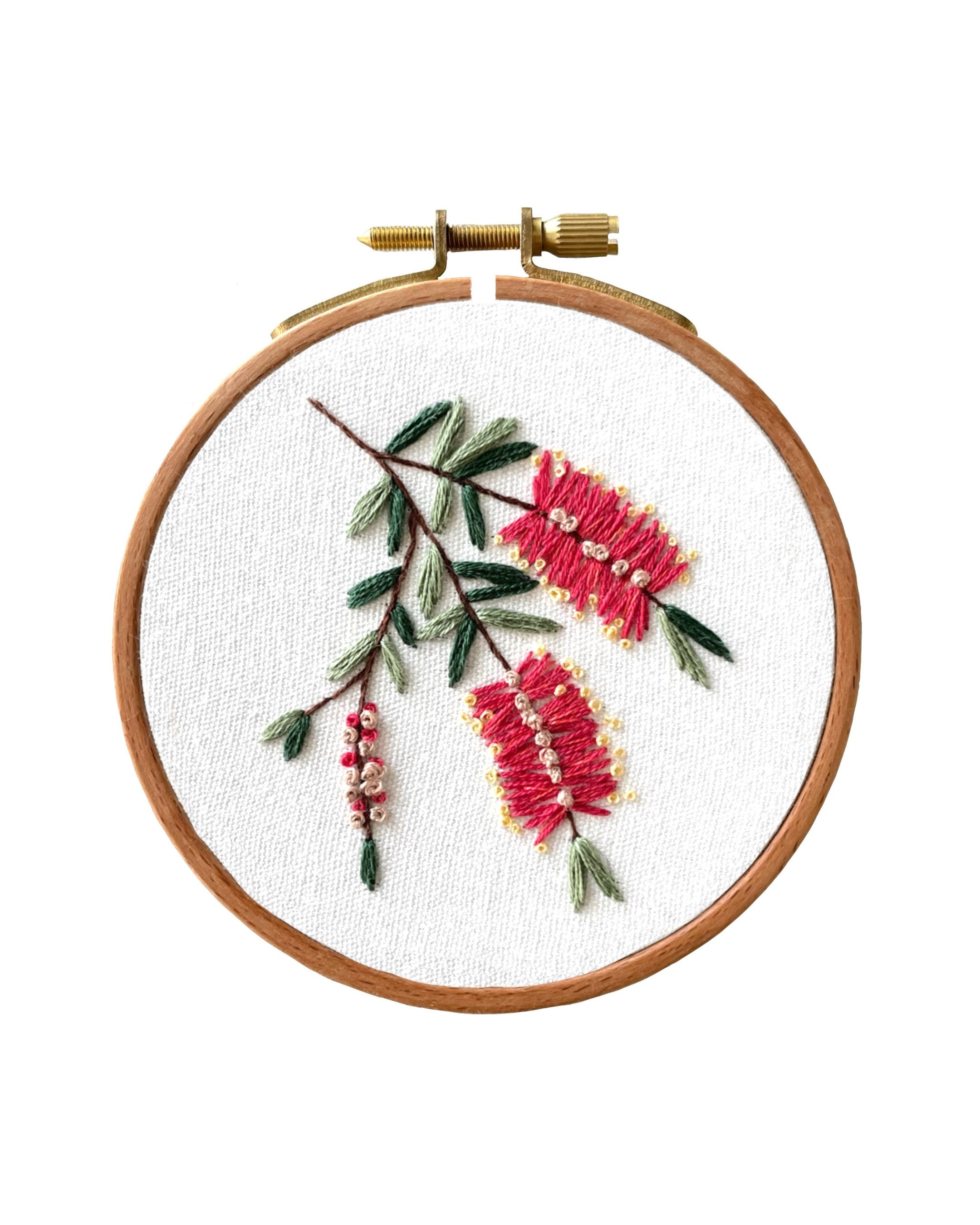 Mini Bottlebrush embroidered on white fabric in wooden hoop featuring pink bottle brush flowers with green foliage and stems