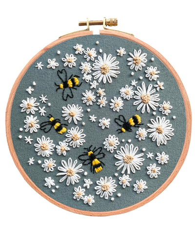 Completed Busy Bumble Bee embroidery Kit on white background. Design is on dark Blue-Grey fabric and has white flowers all over it and 4 bees in amongst them.